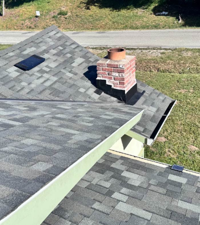Detailed close-up of a perfectly sealed roof flashing installation around a white brick chimney on a newly completed dark grey asphalt shingle roof.