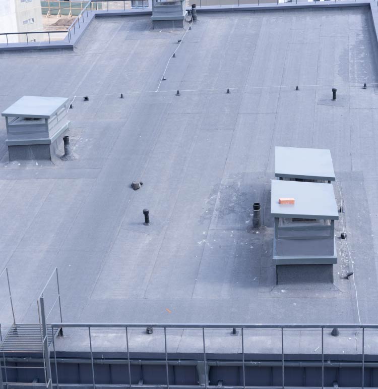 An overhead view of a dark grey commercial flat roof membrane with perimeter safety railings, rooftop service access hatches, and ventilation housings.