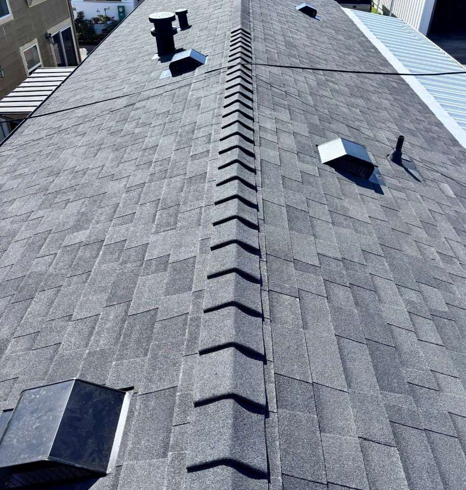 premium-rof Top-down view of a newly finished, clean dark grey asphalt shingle residential roof with professionally installed ridge caps and vents.