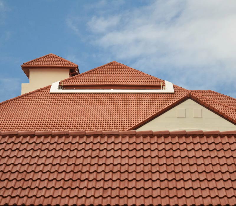 The architectural upper exterior of a luxury home showcasing a pristine, expansive orange concrete tile roofing system with multiple steep hips, ridges, and valleys.