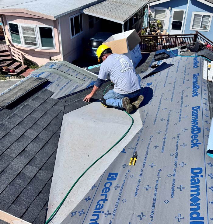 roofer-1 A professional roofer in a yellow hard hat and branded grey shirt carefully laying shingles over a DiamondDeck underlayment base.