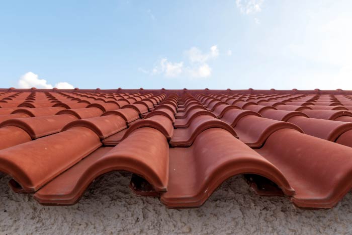 A low-angle, close-up perspective of pristine red clay barrel tiles installed in uniform rows stretching toward a clear blue sky.