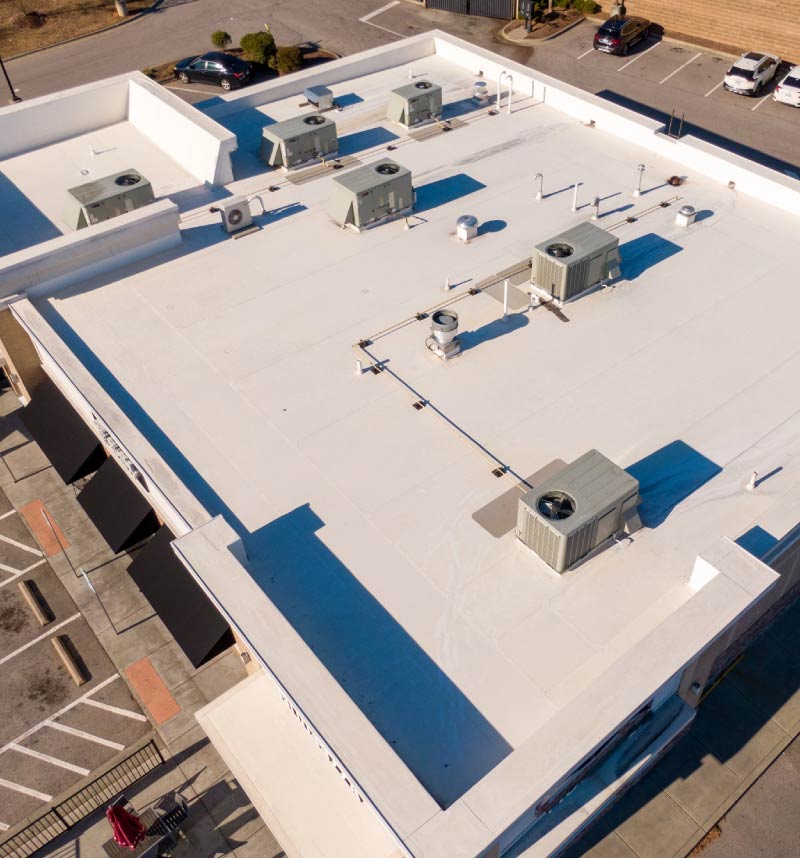 An aerial drone perspective of a clean white commercial flat roof installation featuring multiple integrated HVAC units, ventilation systems, and drainage lines.