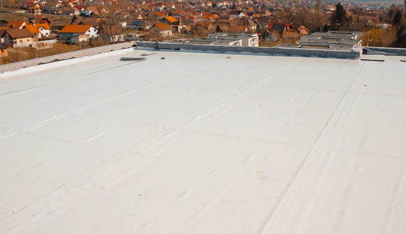 A vast, newly installed white single-ply flat roof membrane on a commercial building overlooking a residential neighborhood.